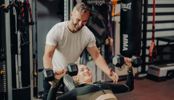 Entrenador personal supervisando a una mujer mientras realiza un press de banca con mancuernas en el gimnasio boutique Trim.